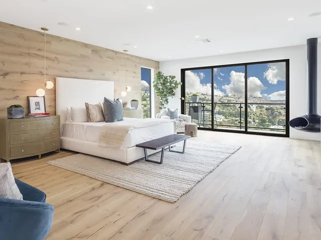 Primary bedroom with a wood accent wall and glass doors opening to a hillside view