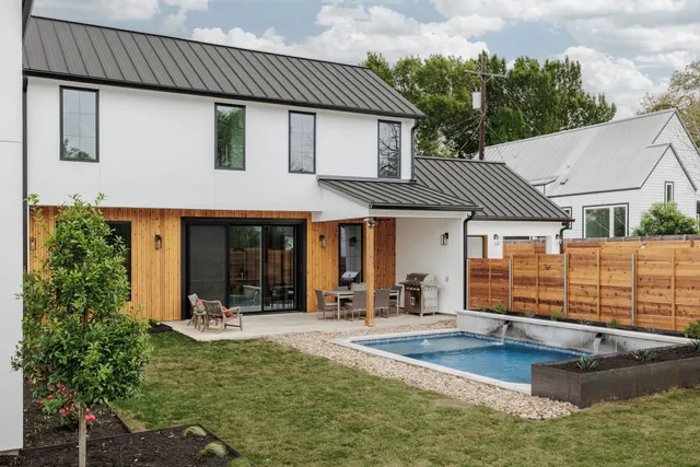 Backyard patio and pool behind a modern white and wood-paneled home