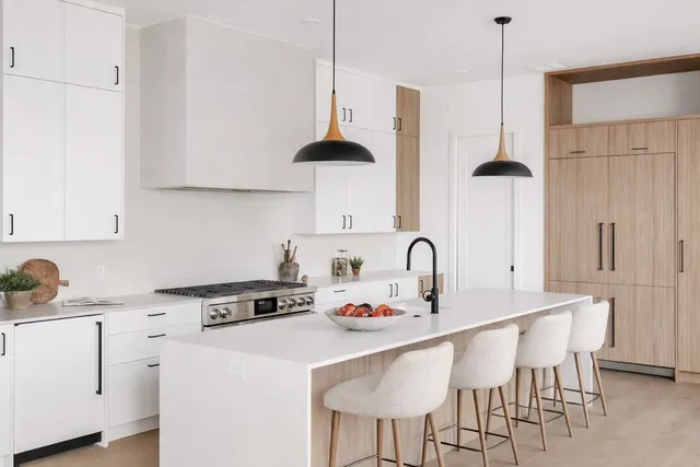 Kitchen with black pendant lights, light wood cabinetry, and tile backsplash