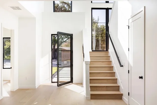 Bright entryway with a wood staircase, black-framed windows, and a pivoting glass front door