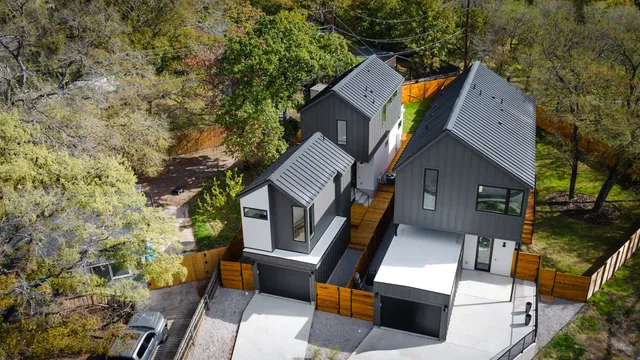 Aerial view of three connected modern homes with standing-seam metal roofs and wood fencing